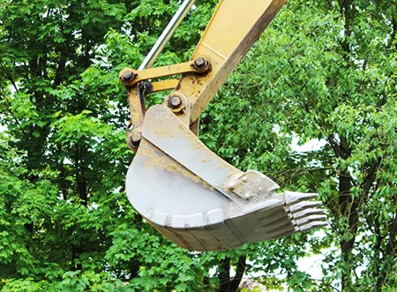 Godet d’excavatrice devant un arrière-plan d’arbres verts.